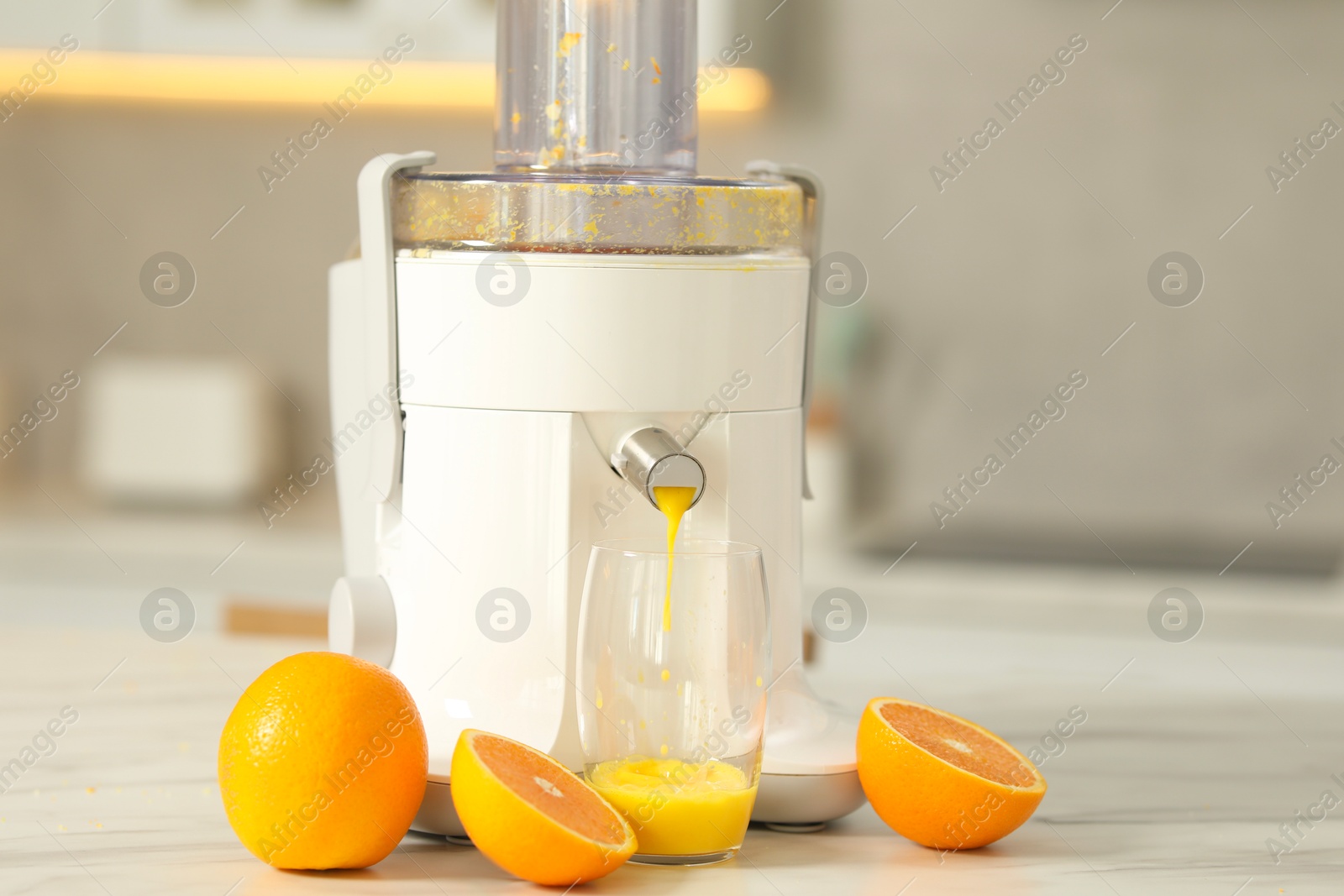 Photo of Modern juicer, oranges and glass on white marble table in kitchen