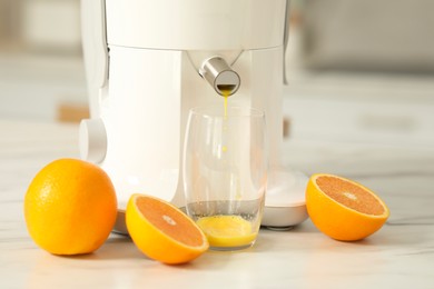 Photo of Modern juicer, oranges and glass on white marble table in kitchen