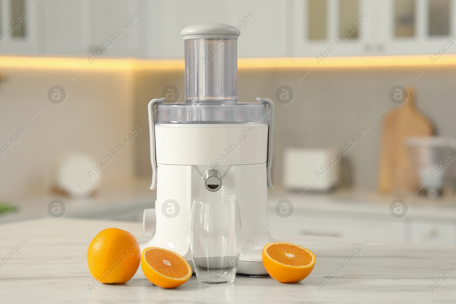 Photo of Modern juicer, oranges and glass on white marble table in kitchen