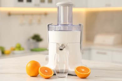 Photo of Modern juicer, oranges and glass on white marble table in kitchen