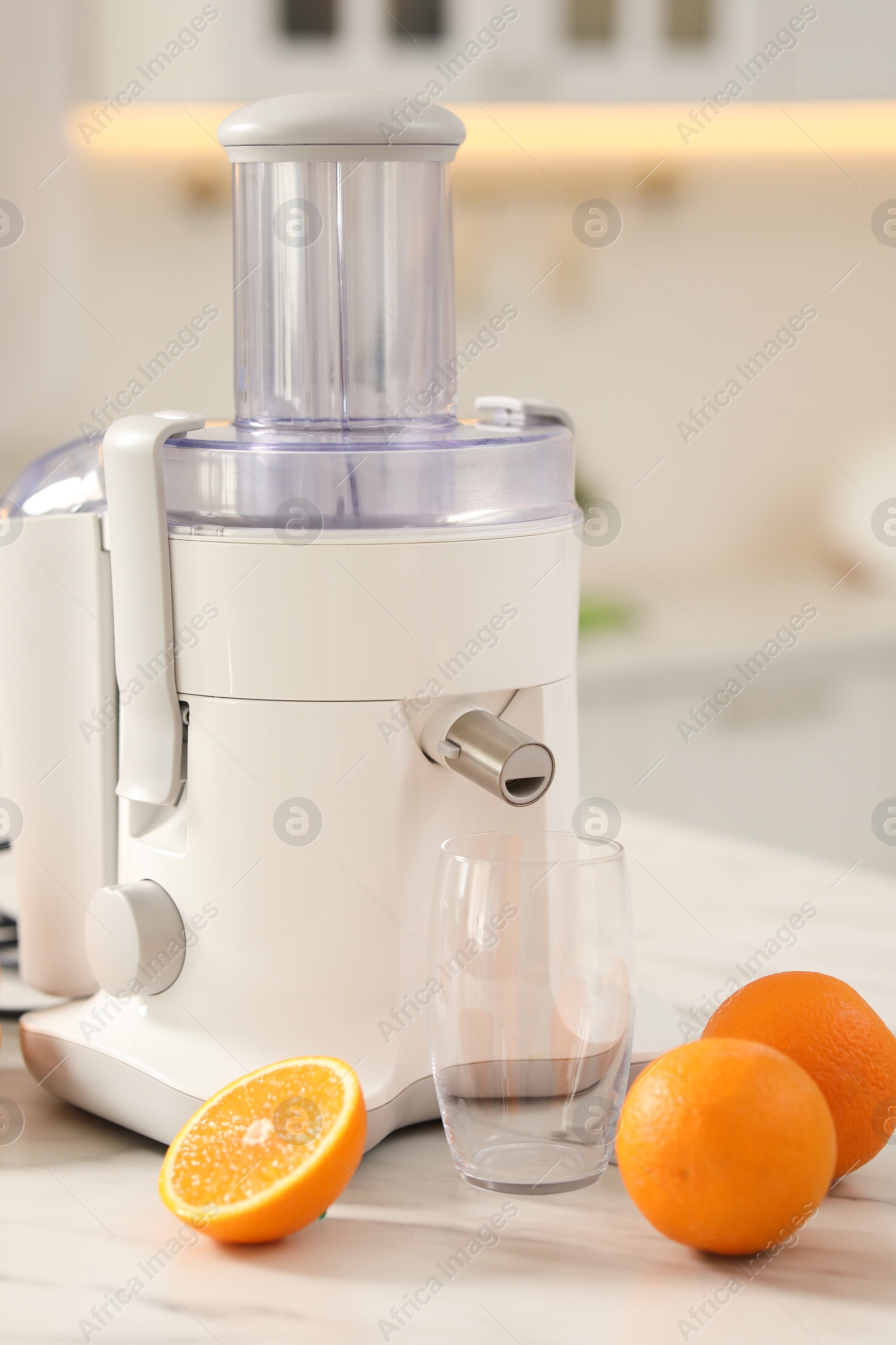 Photo of Modern juicer, oranges and glass on white marble table in kitchen