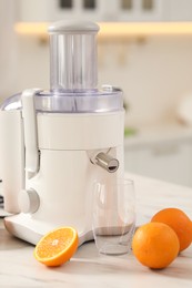 Photo of Modern juicer, oranges and glass on white marble table in kitchen