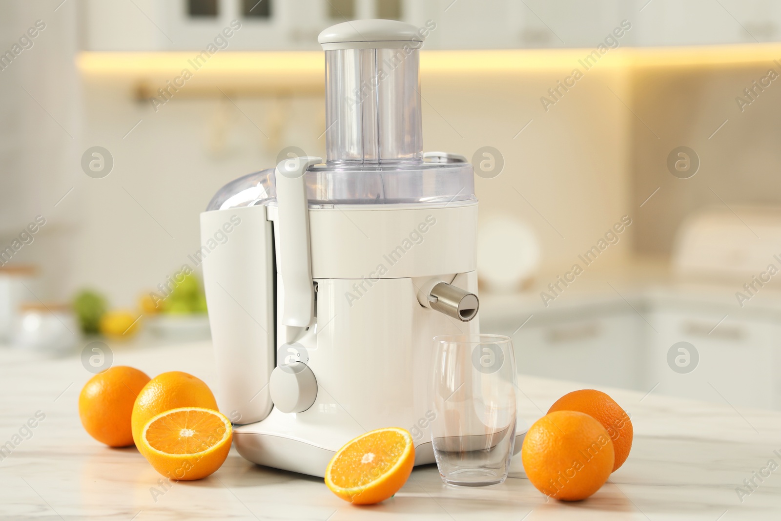 Photo of Modern juicer, oranges and glass on white marble table in kitchen