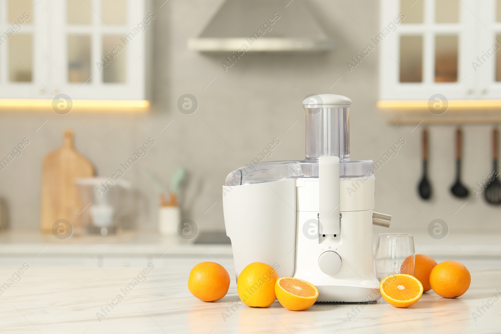 Photo of Modern juicer, oranges and glass on white marble table in kitchen, space for text