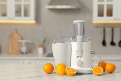 Photo of Modern juicer, oranges and glass on white marble table in kitchen, space for text