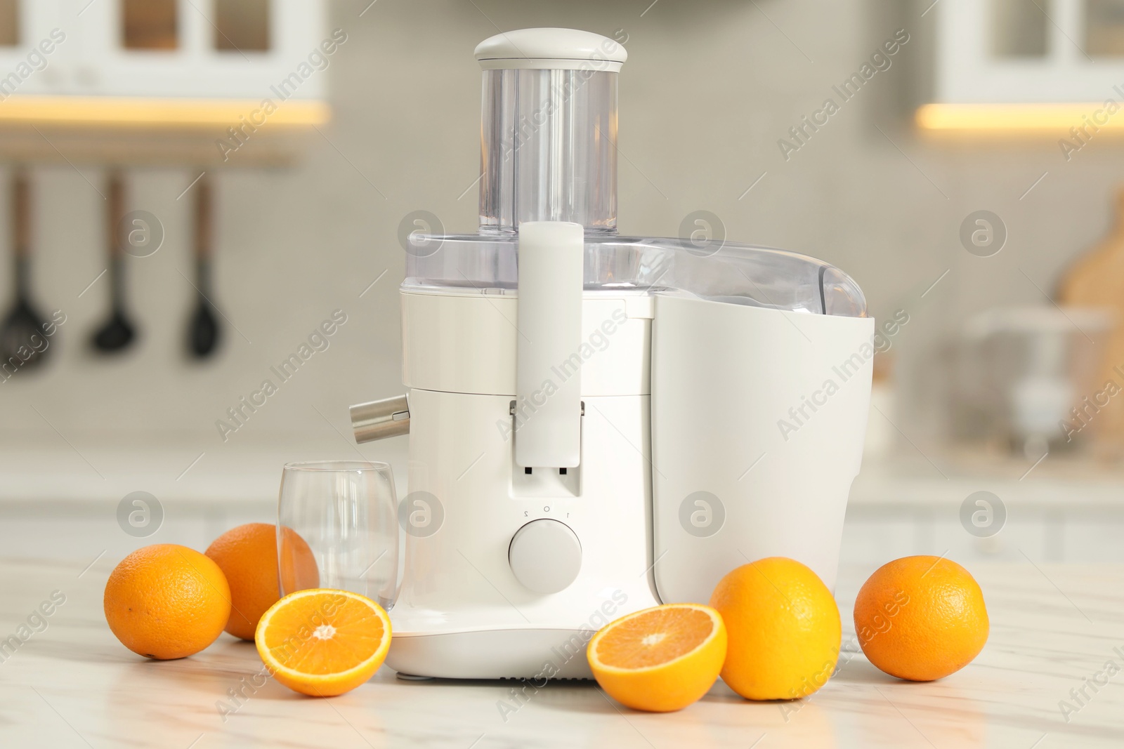 Photo of Modern juicer, oranges and glass on white marble table in kitchen