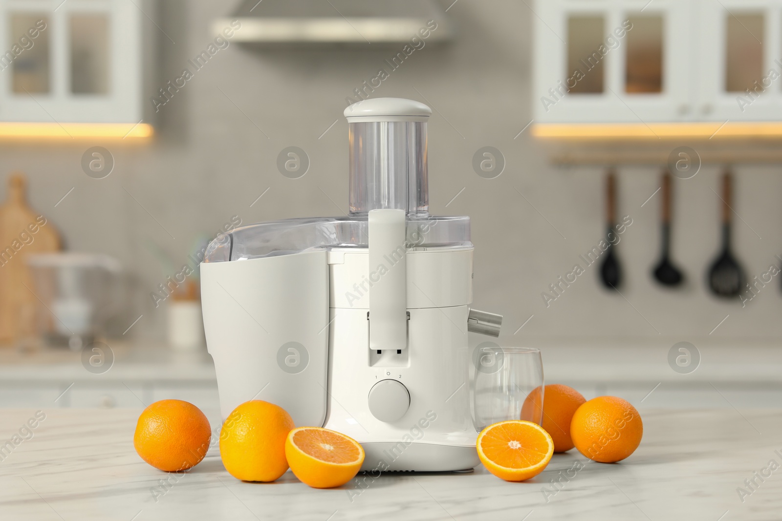 Photo of Modern juicer, oranges and glass on white marble table in kitchen