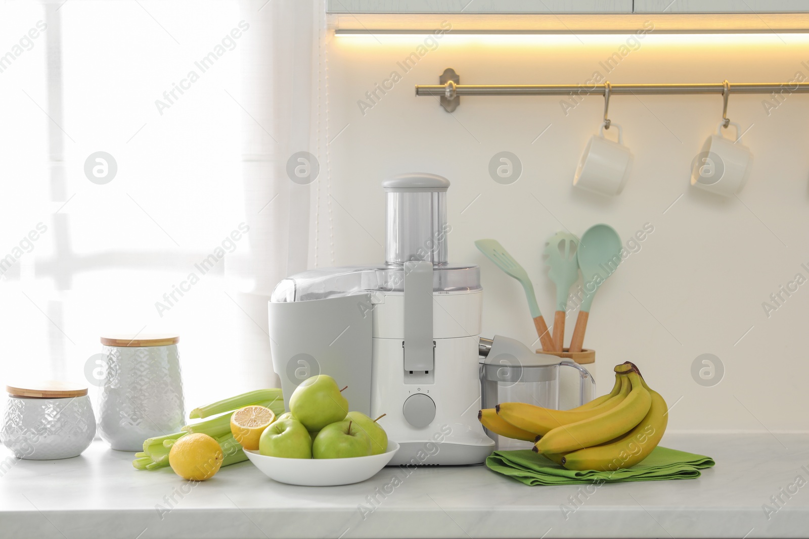 Photo of Modern juicer and fruits on white counter in kitchen