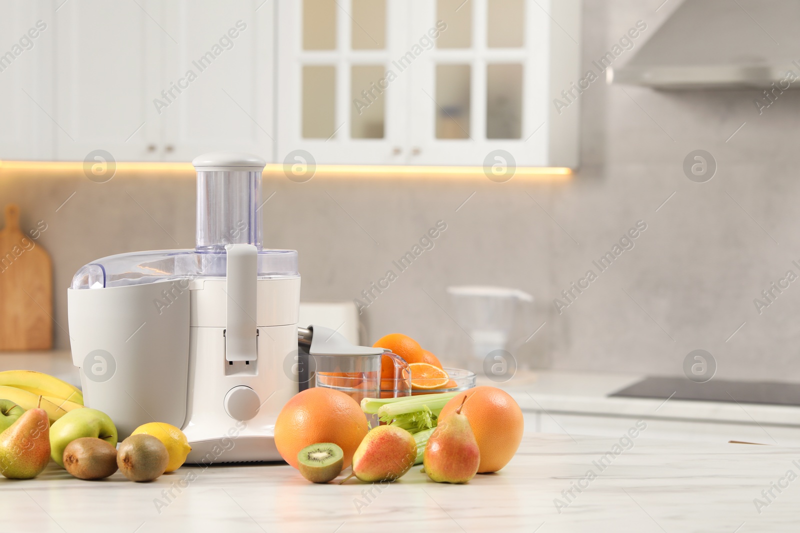 Photo of Modern juicer and fruits on white marble table in kitchen, space for text