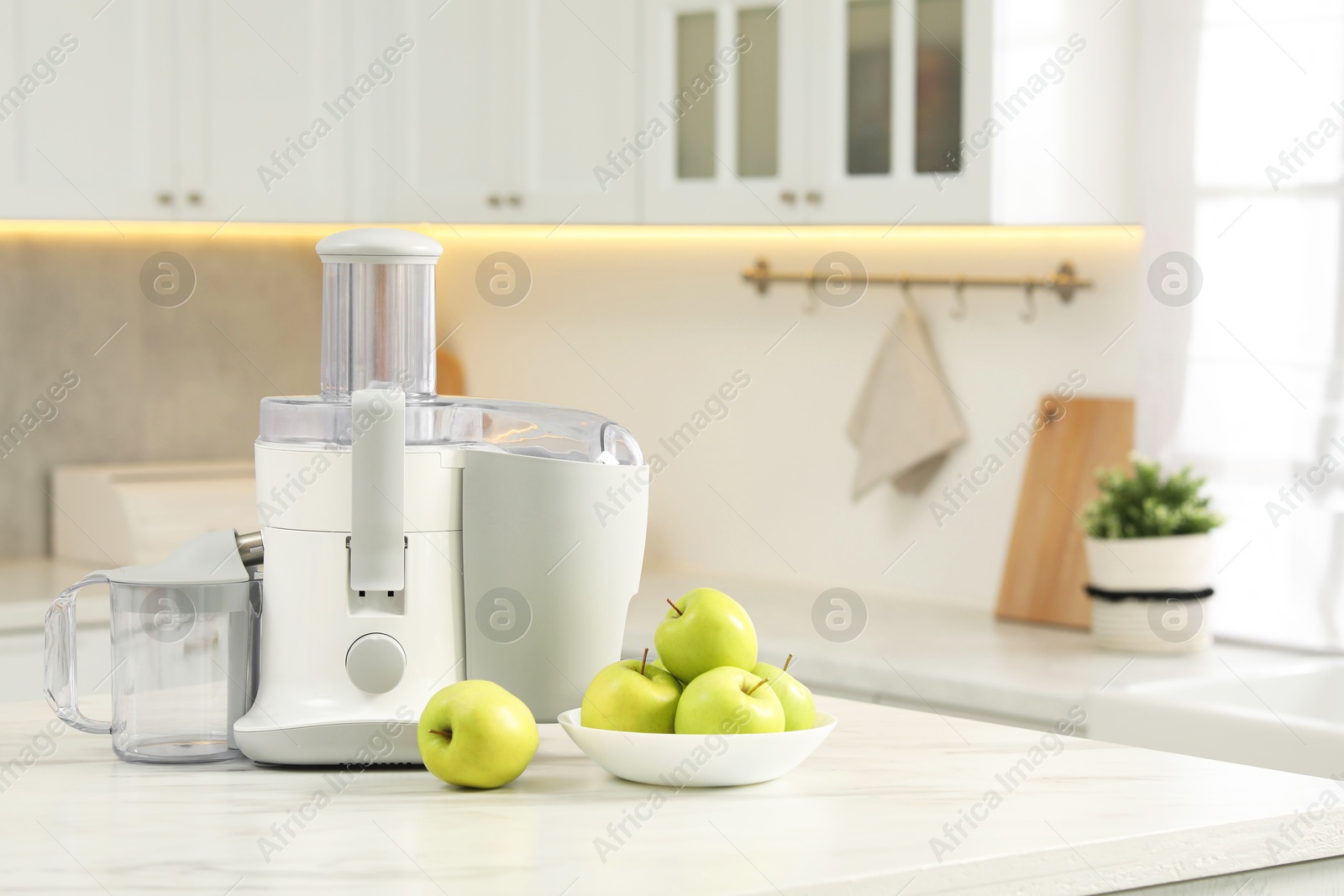 Photo of Modern juicer and apples on white marble table in kitchen, space for text