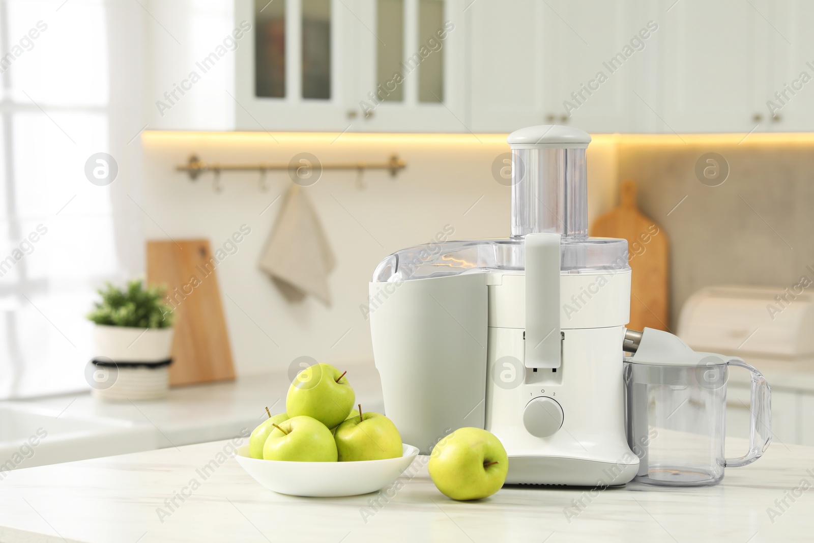 Photo of Modern juicer and apples on white marble table in kitchen, space for text