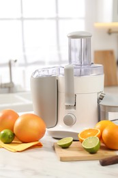 Photo of Modern juicer, oranges and limes on white marble table in kitchen