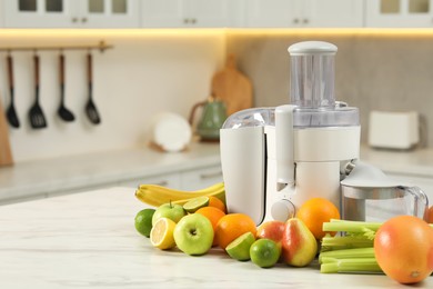 Photo of Modern juicer and fruits on white marble table, space for text