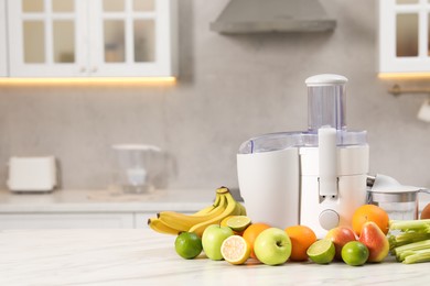 Modern juicer and fruits on white marble table, space for text