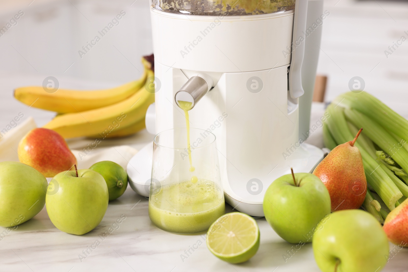 Photo of Modern juicer, fruits and glass on white marble table, closeup