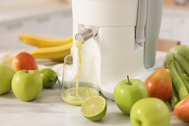 Photo of Modern juicer, fruits and glass on white marble table, closeup