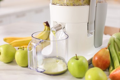 Photo of Modern juicer, fruits and mug on white marble table, closeup