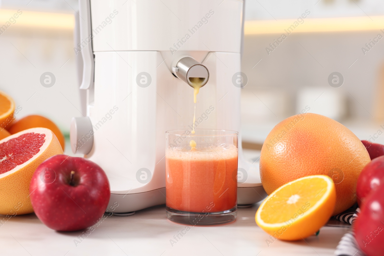 Photo of Modern juicer, fruits and glass on white marble table in kitchen, closeup