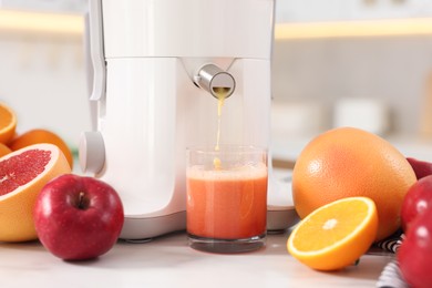 Photo of Modern juicer, fruits and glass on white marble table in kitchen, closeup