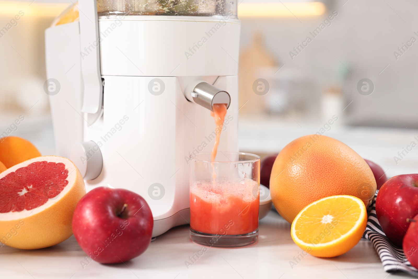 Photo of Modern juicer, fruits and glass on white marble table in kitchen, closeup