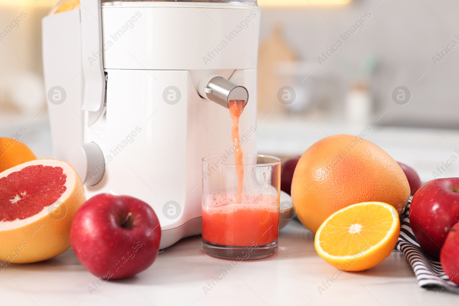 Photo of Modern juicer, fruits and glass on white marble table in kitchen, closeup