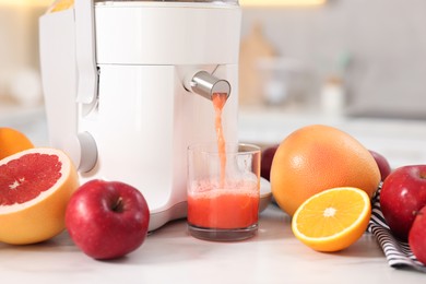 Photo of Modern juicer, fruits and glass on white marble table in kitchen, closeup