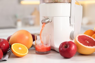 Modern juicer, fruits and glass on white marble table in kitchen, closeup