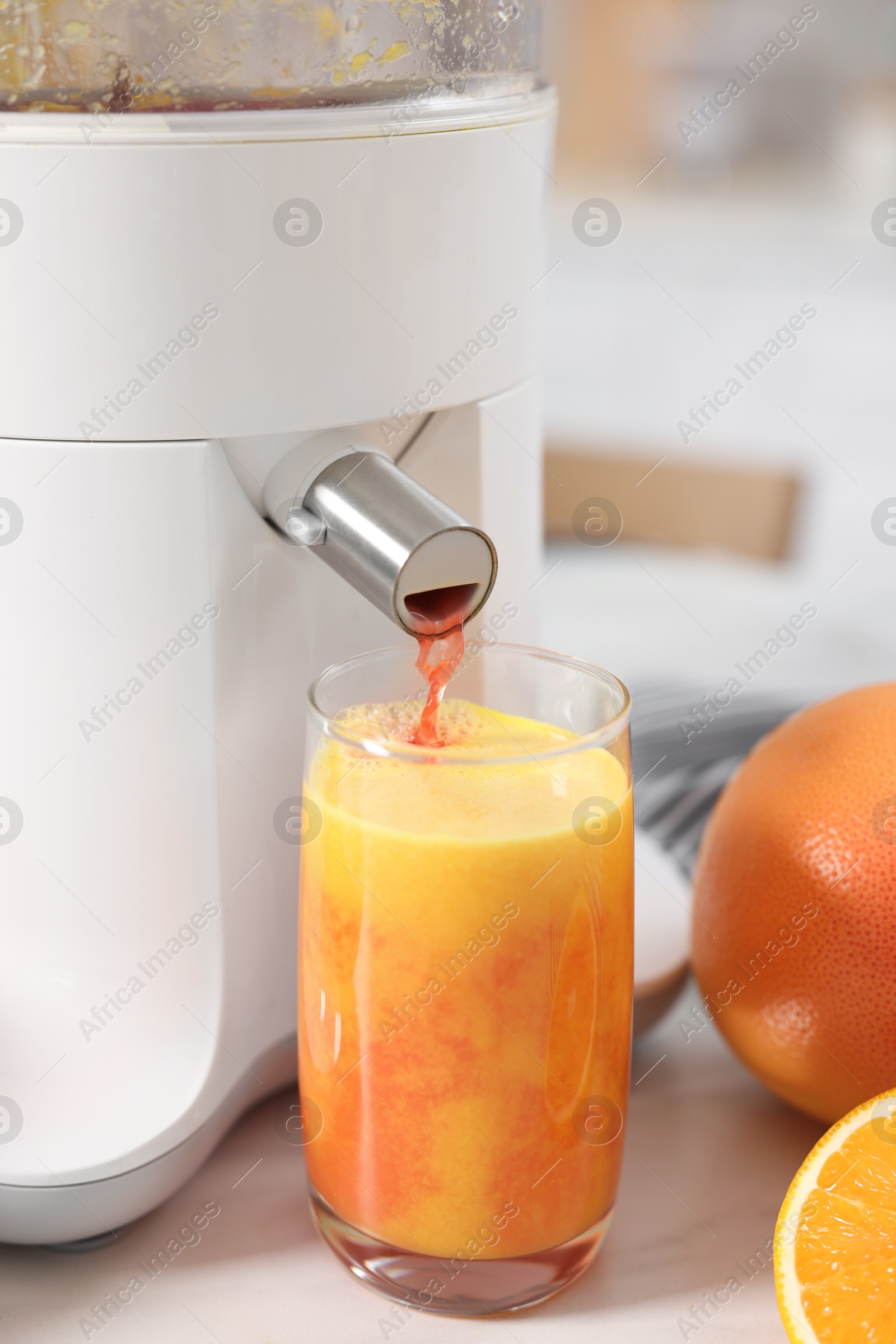 Photo of Modern juicer, oranges, grapefruits and glass on white marble table in kitchen, closeup