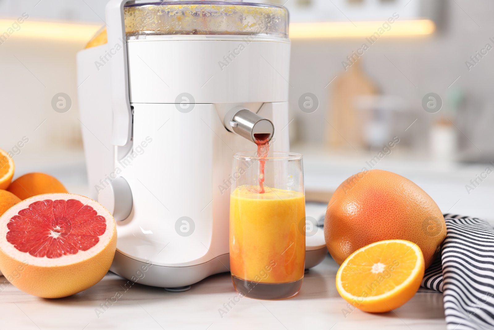 Photo of Modern juicer, oranges, grapefruits and glass on white marble table in kitchen