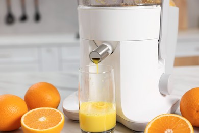 Photo of Modern juicer, oranges and glass on white table in kitchen, closeup