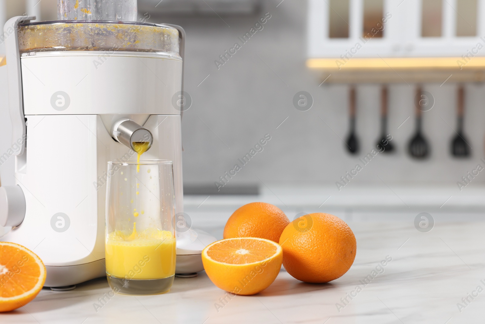 Photo of Modern juicer, oranges and glass on white marble table in kitchen, space for text