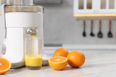 Modern juicer, oranges and glass on white marble table in kitchen, space for text