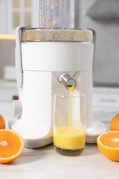 Modern juicer, oranges and glass on white marble table in kitchen