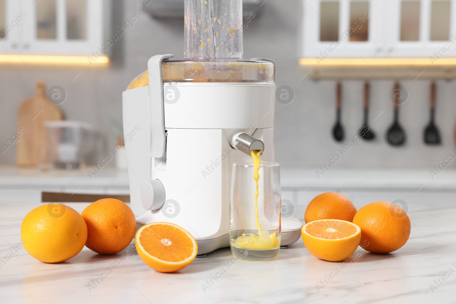 Photo of Modern juicer, oranges and glass on white marble table in kitchen