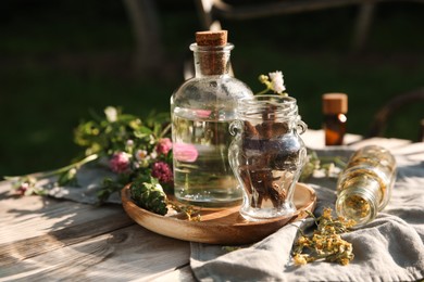 Photo of Tincture in bottle, flowers and pine cone on wooden bench outdoors, closeup