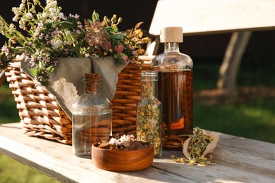 Different tinctures in bottles, bark chips and flowers on wooden bench outdoors