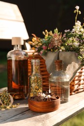 Different tinctures in bottles, bark chips and flowers on wooden bench outdoors