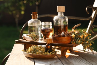 Different tinctures in bottles, bark chips and flowers on wooden bench outdoors