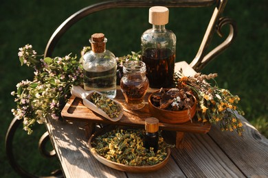 Different tinctures in bottles, bark chips and flowers on wooden bench outdoors