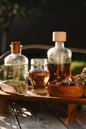 Different tinctures in bottles, bark chips and flowers on wooden bench outdoors, closeup