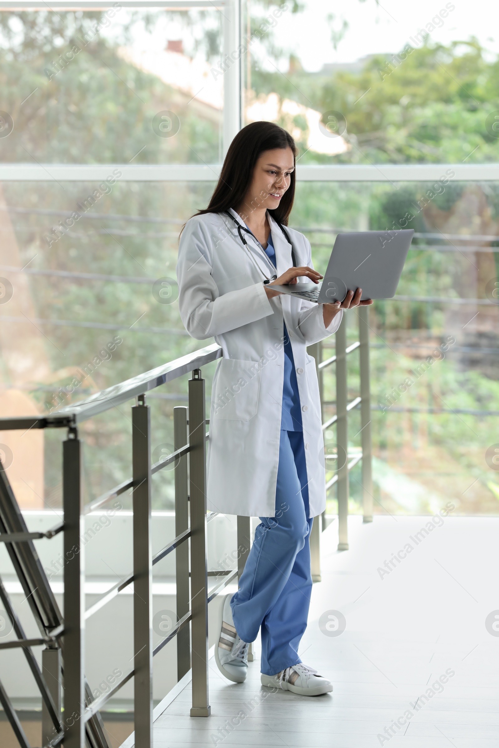 Photo of Smiling nurse with laptop near railings in hospital