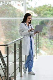 Photo of Smiling nurse with laptop near railings in hospital