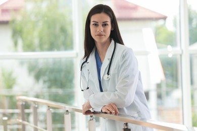 Beautiful nurse with stethoscope near railings in hospital