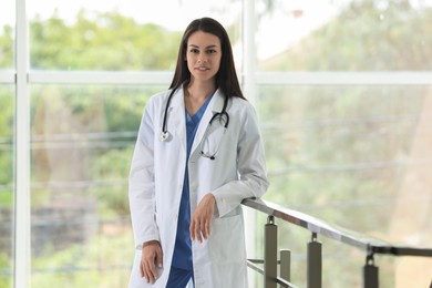 Smiling nurse with stethoscope near railings in hospital