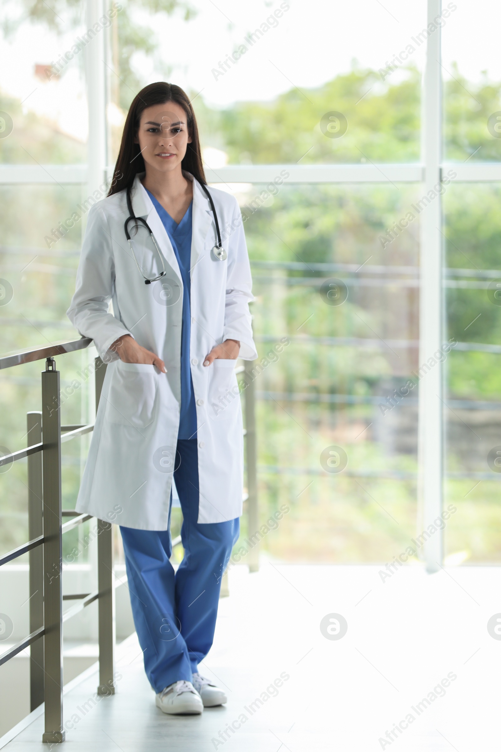 Photo of Smiling nurse with stethoscope near railings in hospital