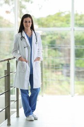 Photo of Smiling nurse with stethoscope near railings in hospital