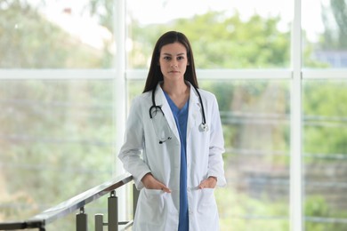 Beautiful nurse with stethoscope near railings in hospital