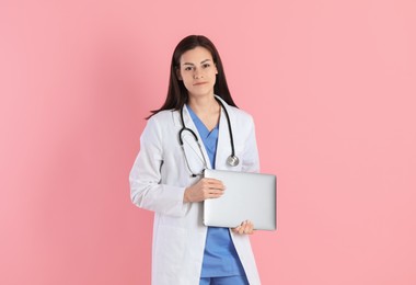 Beautiful nurse with laptop on pink background