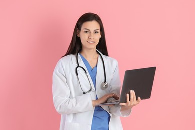 Smiling nurse with laptop on pink background