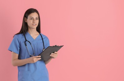 Photo of Smiling nurse with clipboard on pink background. Space for text